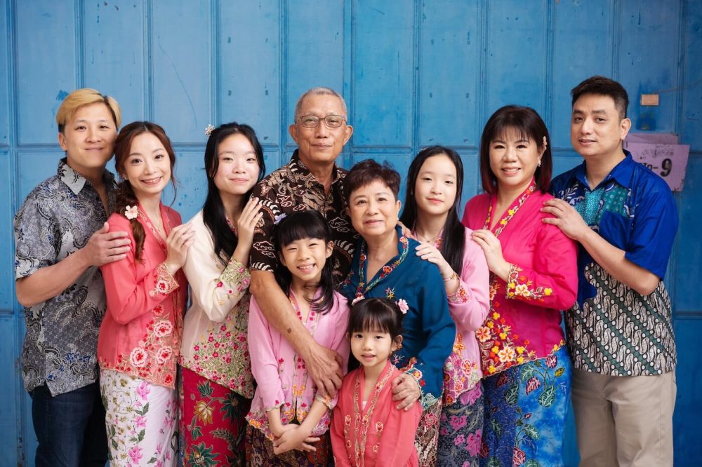 Multi-generation family in Peranakan attire photographed against a life-sized Singapore shophouse backdrop